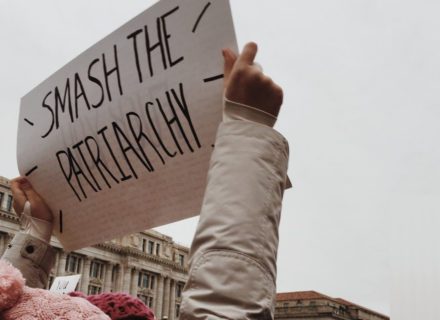 Bildbeschreibung: Ein Schild mit der Aufschrift "Smash the Patriarchy" wir von zwei Kinderhänden in die Luft gehalten.