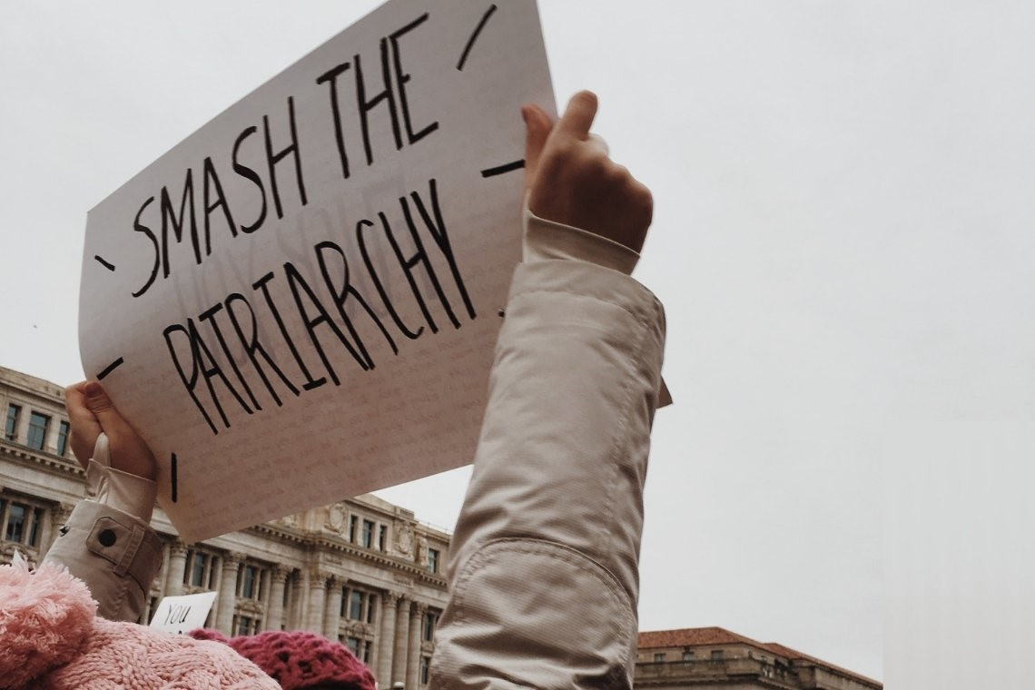 Bildbeschreibung: Ein Schild mit der Aufschrift "Smash the Patriarchy" wir von zwei Kinderhänden in die Luft gehalten.