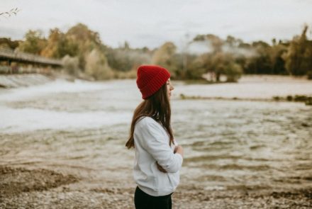 Spirituelles Business aufbauen - enttarnte Mythen & 7 Lehren von meinem Weg [Bildbeschreibung: Eine junge Frau mit einer auffallenden roten Mütze steht an einem Flussufer und scheint in die Ferne zu schauen]