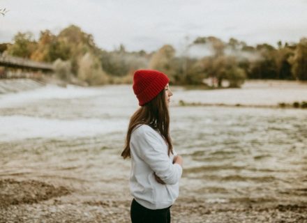 Spirituelles Business aufbauen - enttarnte Mythen & 7 Lehren von meinem Weg [Bildbeschreibung: Eine junge Frau mit einer auffallenden roten Mütze steht an einem Flussufer und scheint in die Ferne zu schauen]
