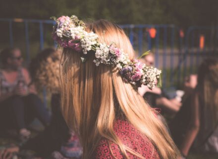 Beitragsbild zum Blogbeitrag "Sommersonnenwende Rituale – erstrahle in Deiner Lebenskraft!" von Suzanne Frankenfeld. Bildbeschreibung: Man sieht von der Seite den Kopf und Oberkörper einer jungen weiblich gelesenen Person. Sie trägt einen Blumenkranz auf dem Kopf. Die Sonne fällt auf ihr Haar.