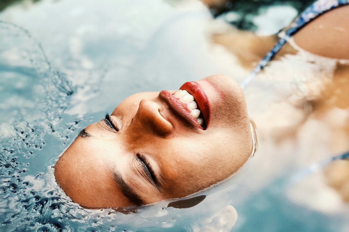 Hochsensibel energetischer Schutz – Beitragsbild zum Blogbeitrag "Brauchen Hochsensible energetischen Schutz?" von Suzanne Frankenfeld. Auf dem Bild zu sehen ist das Gesicht einer im Wasser liegenden Frau sehr nah fotografiert. Die Frau hat die Augen geschlossen und lächelt. Sie sieht freudvoll und entspannt aus.