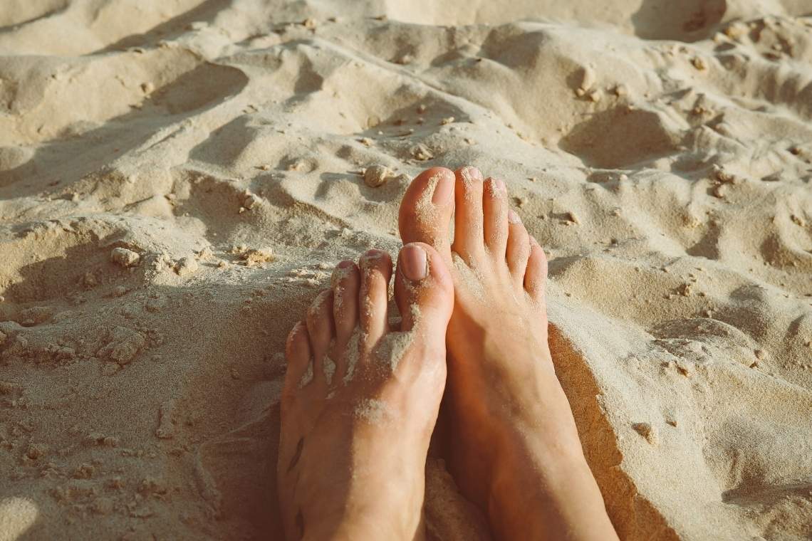 Nackte Füße im Sand, im Sonnenschein.