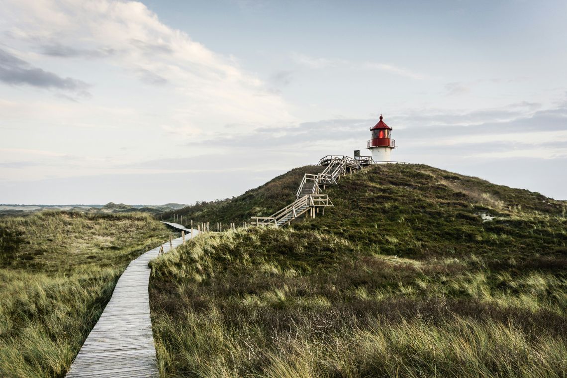 Ein Bohlenweg führt durch Dünen zu einem Seezeichen hin. Aufgenommen auf Amrum.